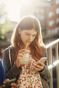 Close-up of a young woman drinking water from mobile phone outdoors