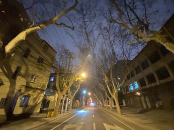 Illuminated street amidst buildings against sky at night