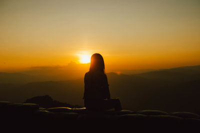 Silhouette of man sitting against orange sky