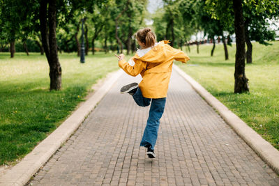 A teenage girl walking in the park jumping with ice cream in her hands. view from the back.