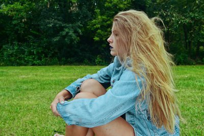 Side view of thoughtful young woman sitting on field at public park