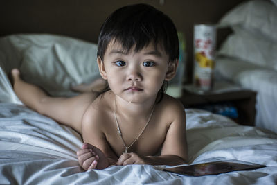 Portrait of naked boy lying on bed at home