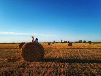 Woman lying on hay bale against sky