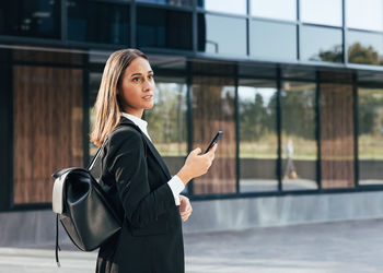Portrait of young woman standing against building