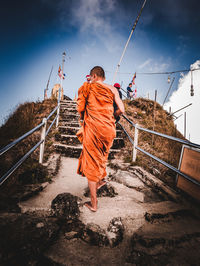 Rear view of man walking on railing against sky