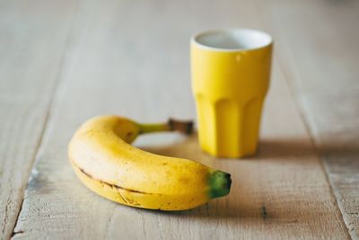 Banana and yellow drinking glass on table