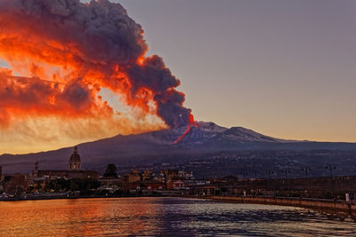 Illuminated buildings in the city during etna eruption