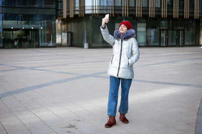 Young woman in a warm jacket communicates online by phone on the street