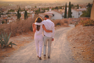 Full length of young couple on dirt road in city at sunset