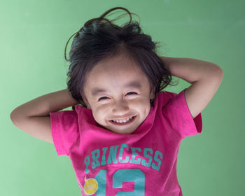 Smiling girl with hands behind head against green background