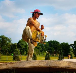 Man with skateboard at park against sky