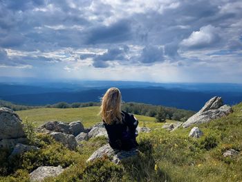 Rear view of woman sitting on rock against sky