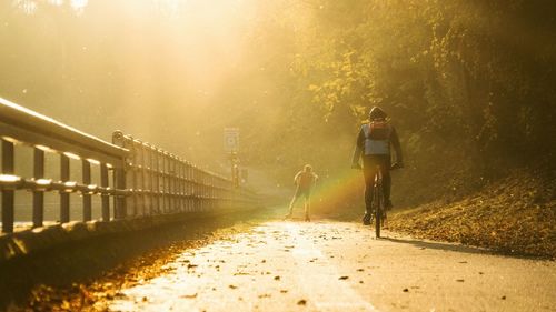 Rear view of man skating with friend riding bicycle on road during sunny day