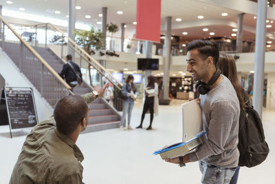 Smiling man looking at student showing direction at corridor in university