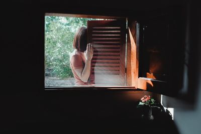 Rear view of woman looking through window at home