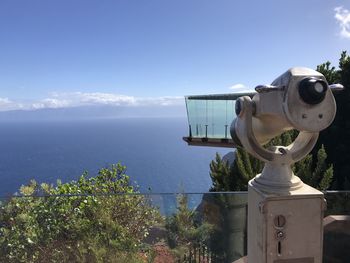 Coin-operated binoculars by sea against sky