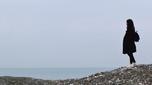 Man standing on rock by sea against clear sky