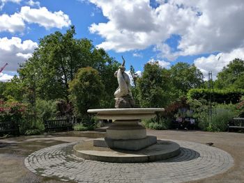 Statue by fountain in park against sky