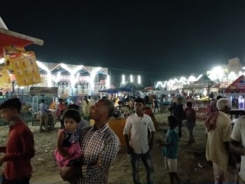 People standing in illuminated city against sky at night