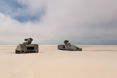 Abandoned armored tanks at desert against cloudy sky