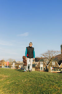 Grandfather standing with granddaughter on grassy field against blue sky