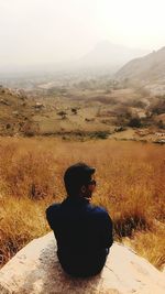 Rear view of man sitting on landscape against sky