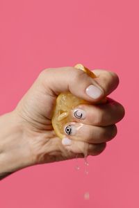 Close-up of hand squeezing lemon over pink background