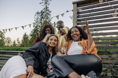 Portrait of woman showing peace sign while enjoying with male and female friends during party in back yard