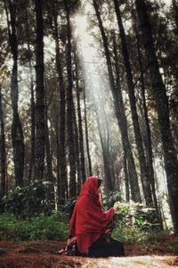 Woman sitting against trees in forest