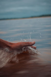 Close-up of hand by sea against sky