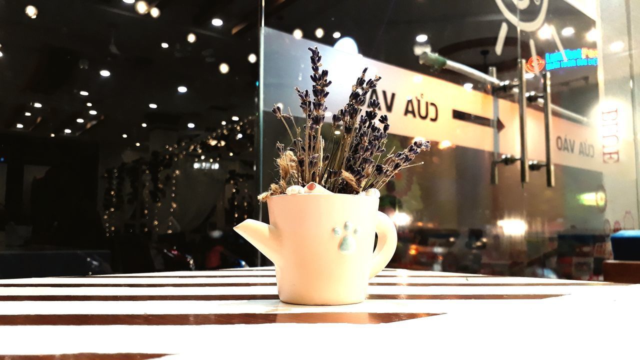 CLOSE-UP OF COFFEE CUP ON TABLE IN ILLUMINATED ROOM