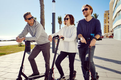 Friends using push scooters in city on sunny day