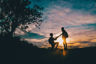 Silhouette friends standing by tree against sky during sunset