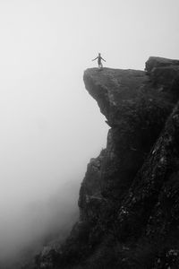 Silhouette man with arms outstretched standing on cliff in foggy weather