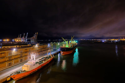 Panoramic view of illuminated harbor by sea against sky at night