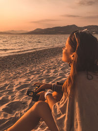 Woman relaxing on beach against sky during sunset