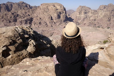 Rear view of mature woman wearing hat sitting on rock formation during sunny day