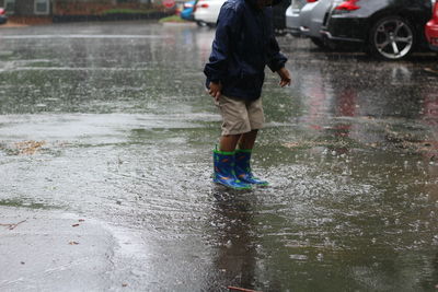 Low section of boy standing in puddle collected on road