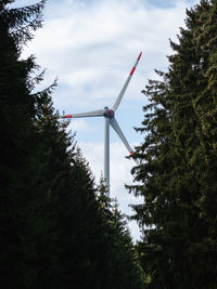 Low angle view of wind turbine and trees against sky