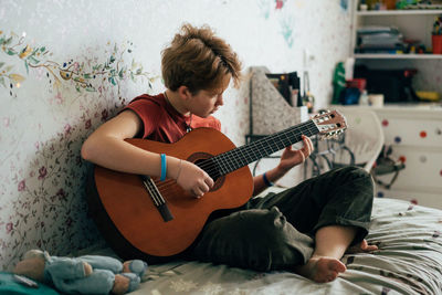 Romantic adolescent redhead girl learning to play the guitar while sitting in the room.