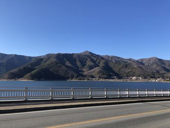 Scenic view of road by mountains against clear blue sky