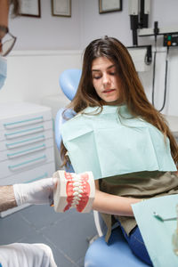 Professional doctor demonstration process of healthy teeth brushing to young woman sitting in chair.