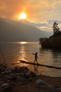 Teenager boy standing at lakeshore during sunset