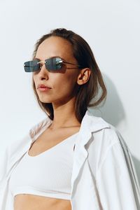 Portrait of young woman wearing sunglasses against white background