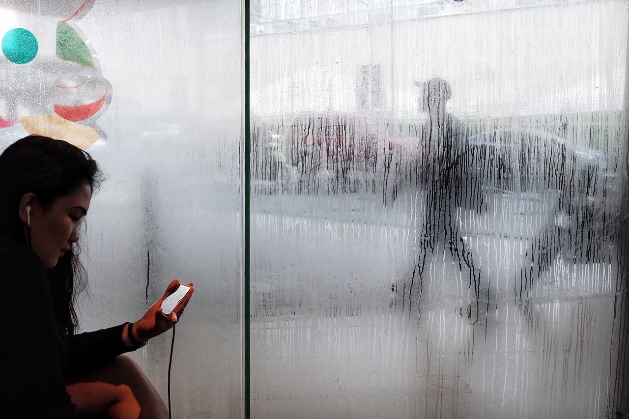 YOUNG WOMAN LOOKING THROUGH WINDOW WHILE SITTING IN GLASS