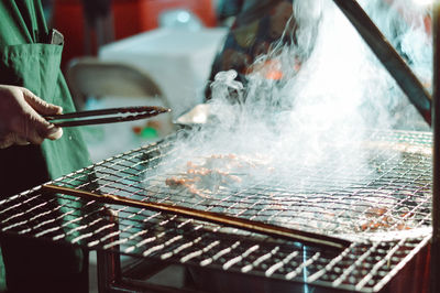 Midsection of person cooking meat on barbecue grill