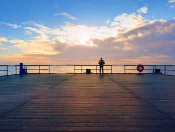 Alone man on pier and look over handrail into water. sunny day. vivid and strong vignetting effect