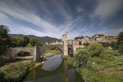 Arch bridge over river against cloudy sky