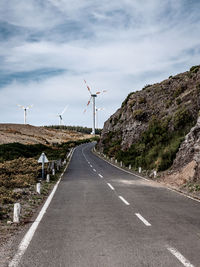 Road by wind turbines against sky