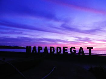 Silhouette text on beach against sky at sunset